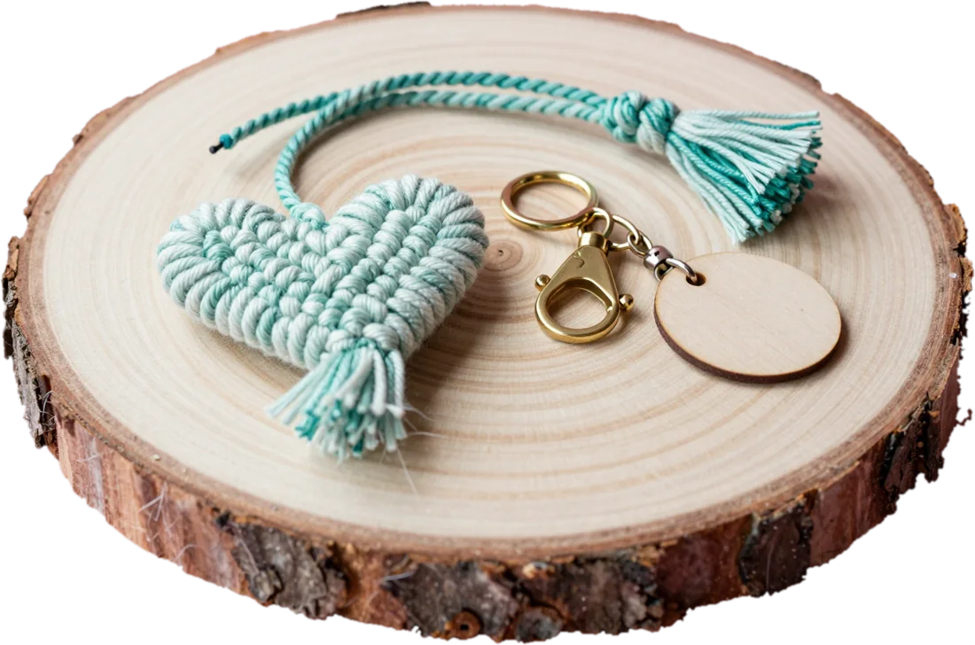 A wood log slice on an oak table with a mint macramé heart, coiled cord, a brass keyring and a blank wooden tag.